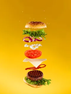 Dekonstruierter Burger mit vielen Zutaten, die durch die Luft fliegen