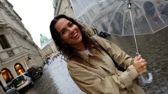 Junge Frau mit Regenschirm in Regenjacke auf nasser Straße in Wiener Innenstadt